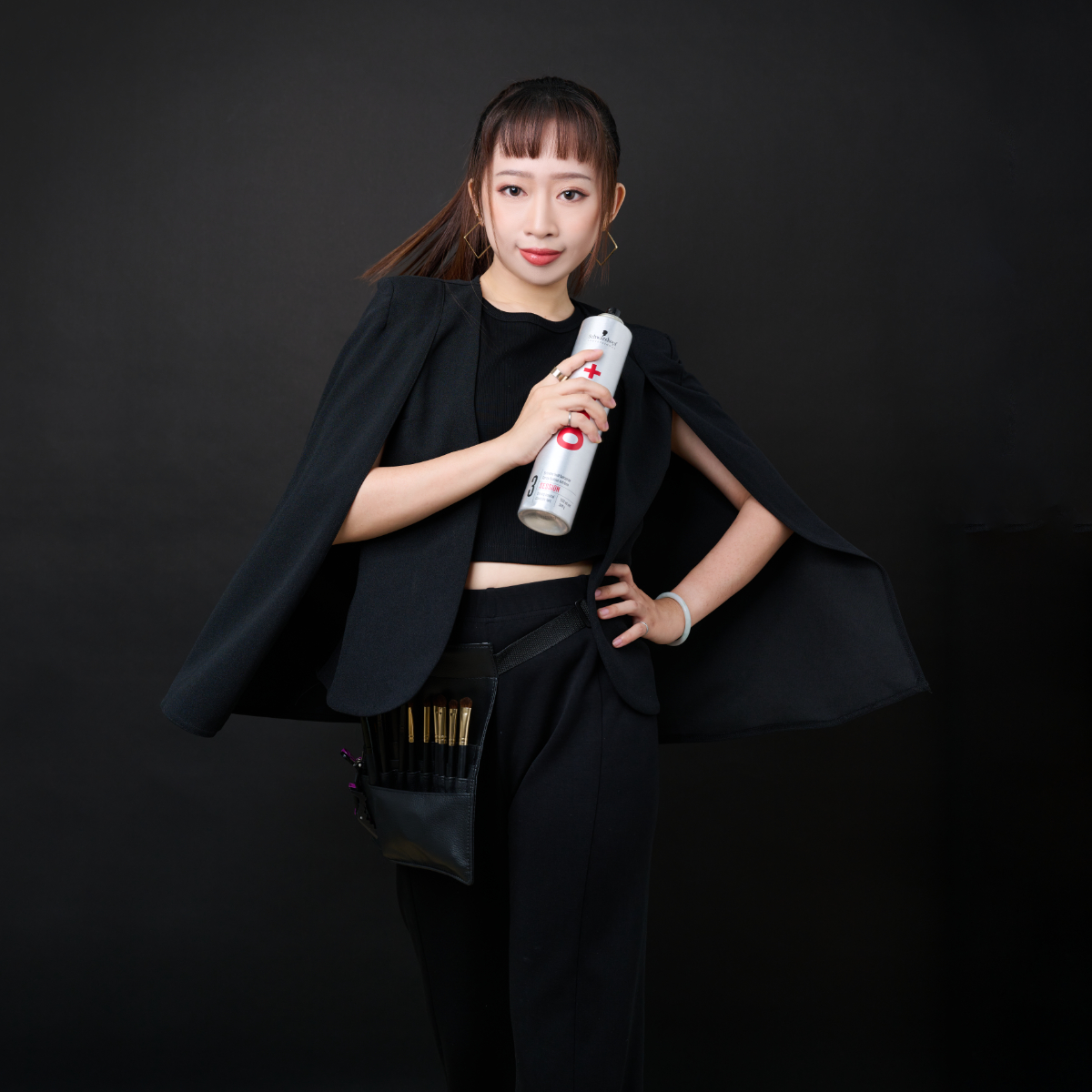 台南造型師形象照:專業新秘/美髮師身穿黑色西裝披肩,配戴專業刷具腰包並手持美髮噴霧,展現俐落、自信與時尚感兼具的職人形象。適合美容產業、新秘教學或時尚造型品牌官網。