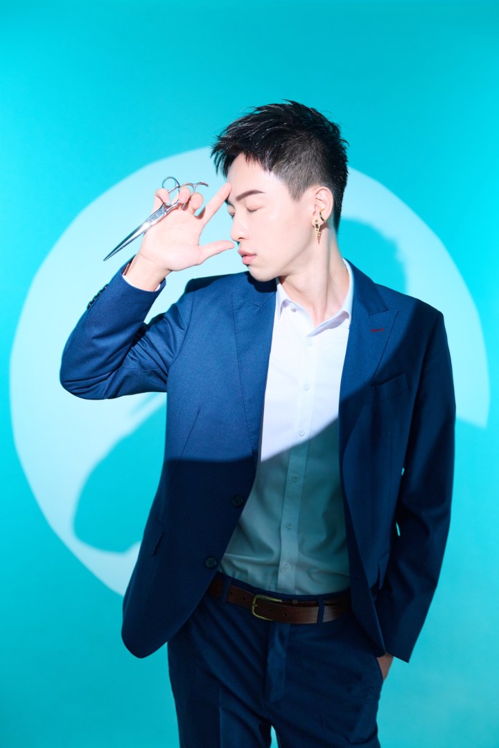 男性理髮師專業形象，背景透過色燈與投影搭配理髮剪刀與西裝外套配色，凸顯理髮師的專業與自信。
