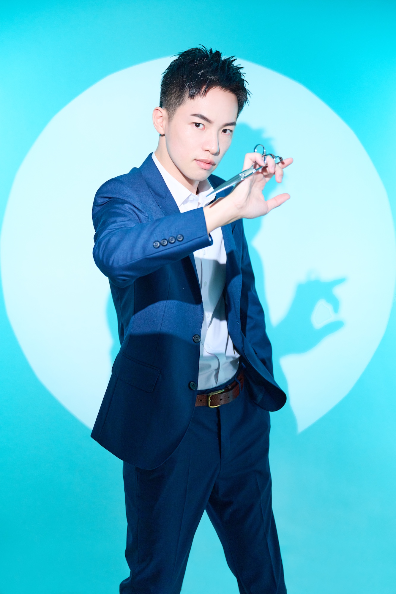 男性理髮師專業形象，背景透過色燈與投影搭配理髮剪刀與西裝外套配色，凸顯理髮師的專業與自信。