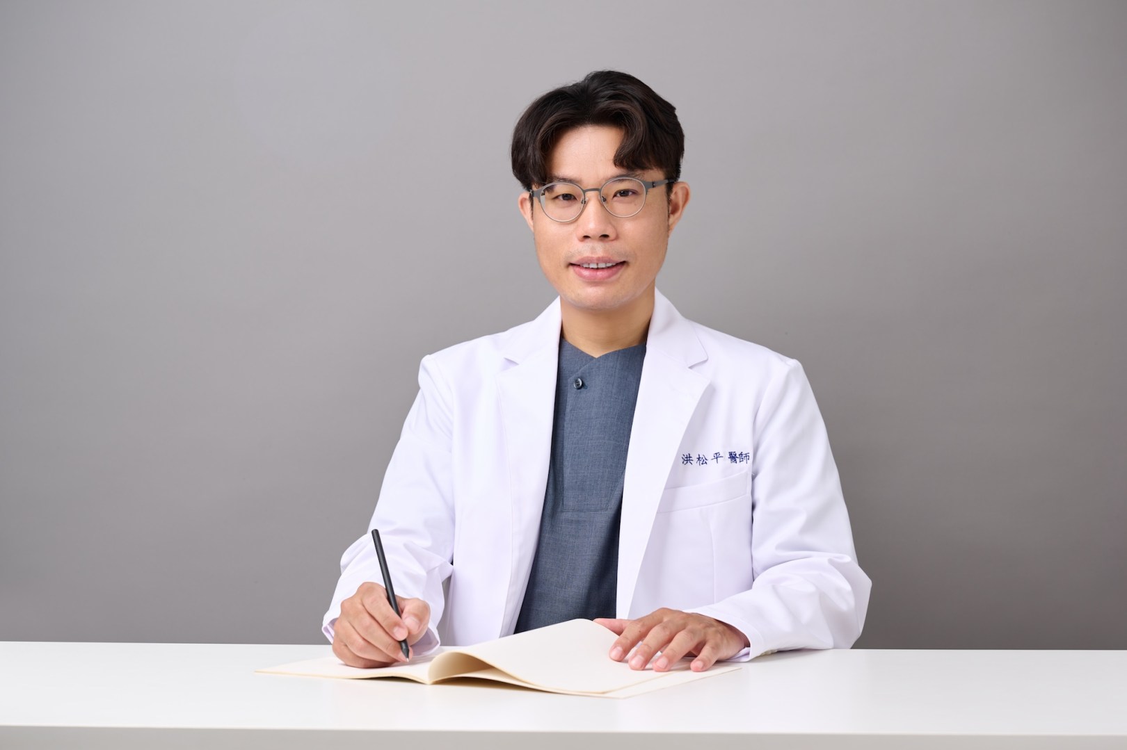台南專業醫師形象照：醫師身穿白袍在桌前專注研讀與筆記，展現嚴謹且具權威感的學術形象。適合醫學網站背景圖、講師介紹與專業形象規劃。