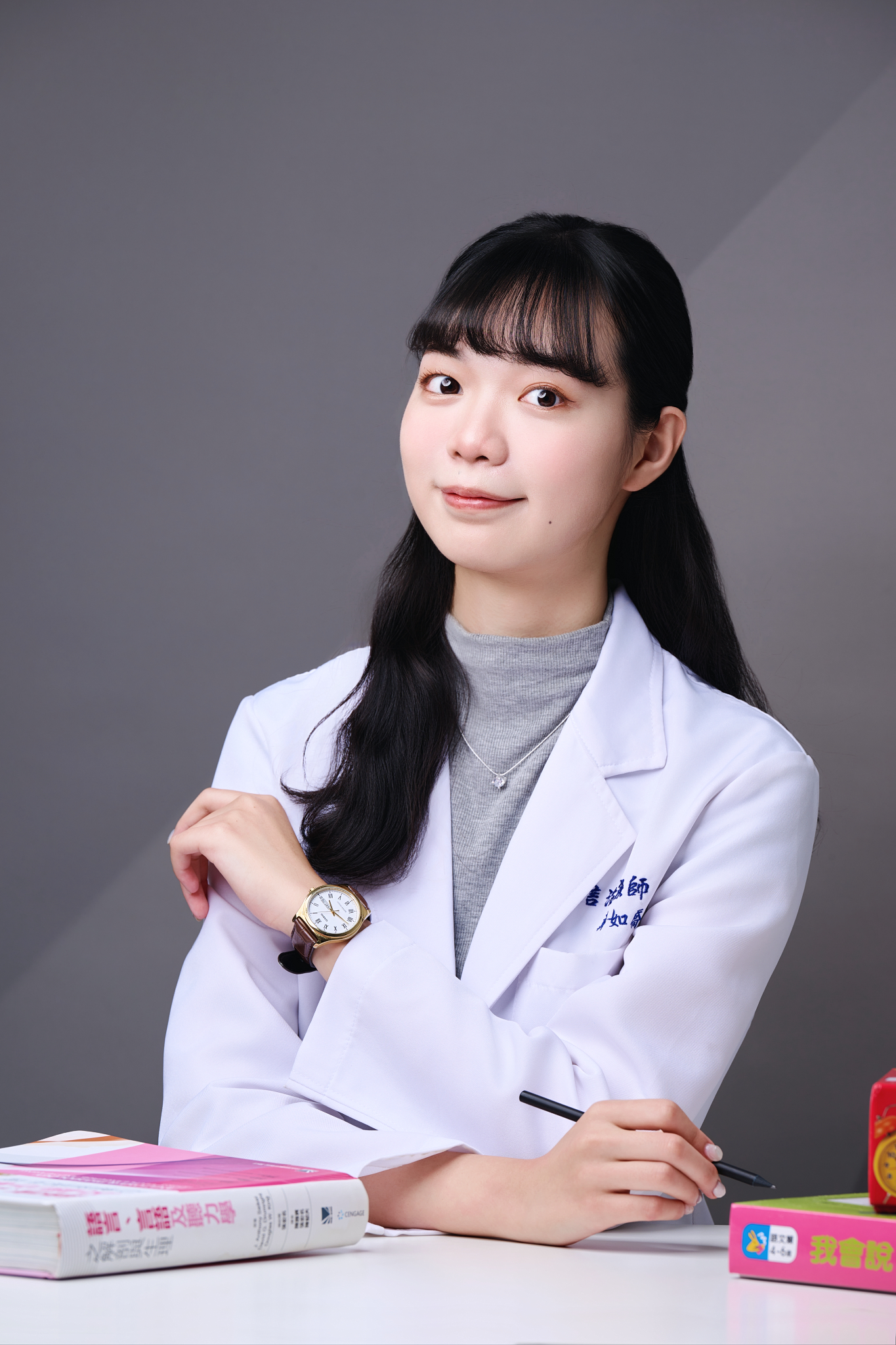 台南語言治療師形象照推薦：治療師於諮詢桌前展現親和微笑與專業知性神韻。畫面結合專業書籍與手寫筆，傳遞嚴謹且平易近人的診療氛圍，適合診所諮詢流程介紹、師資資歷說明與醫療品牌宣傳。