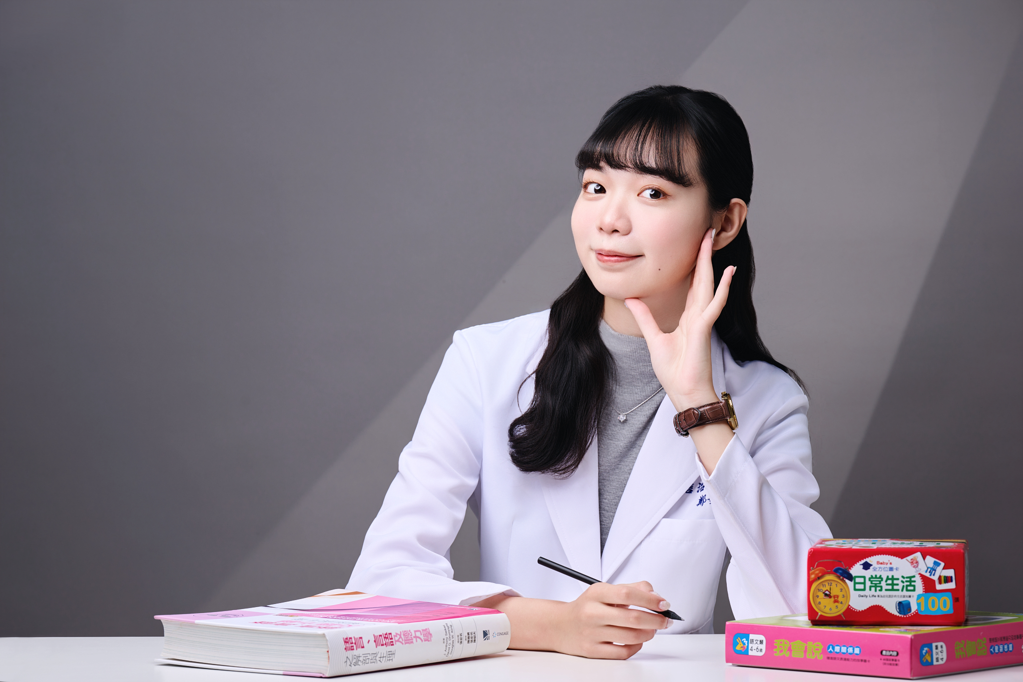 台南語言治療師形象照：治療師坐在桌前，結合專業原文書與教學教具，展現知性、專業且具備親和力的診療形象。適合診所官網醫師簡介、專業專欄首圖與家長諮詢導讀素材。