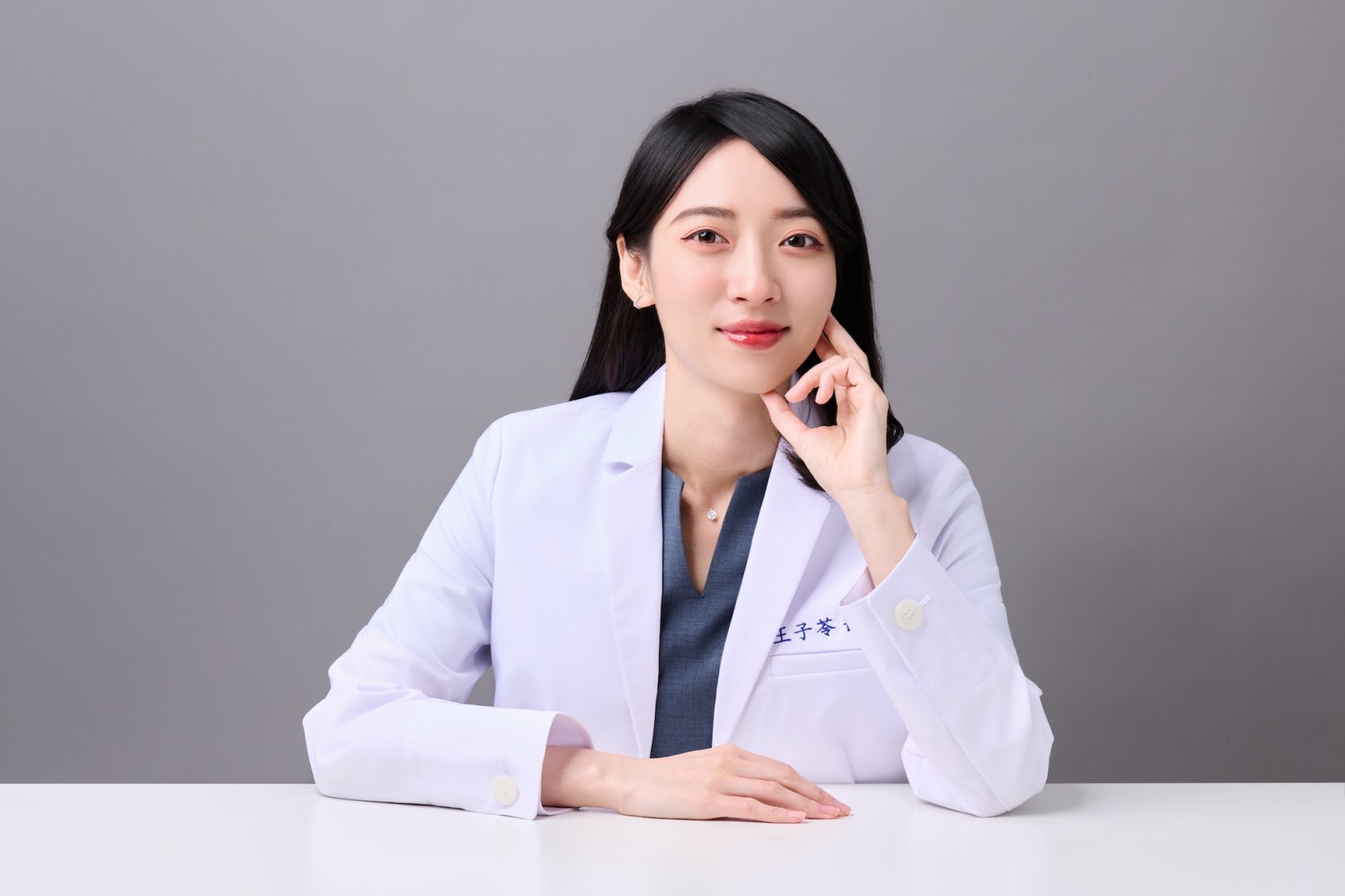 台南中醫師形象照推薦：蒔見中醫醫師坐在桌前，以托腮姿勢展現知性且具親和力的診療形象。適合診所官網醫師簡介、專業專欄首圖與醫病溝通視覺素材。