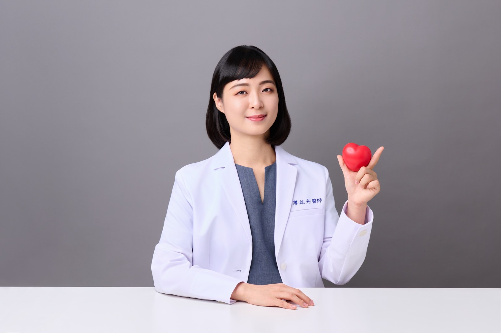 台南中醫師形象照推薦：蒔見中醫醫師坐在桌前展示愛心模型，展現溫暖、知性且具備高度同理心的專業形象。適合診所官網理念介紹、醫病關係專欄與個人品牌形象宣傳。