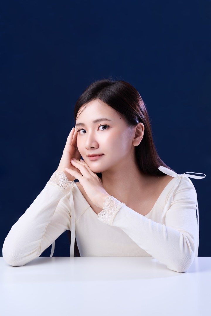 台南形象照首選：熱銷款韓系精緻肖像。長髮女性身穿白色蕾絲袖上衣，以優雅雙手托腮姿勢展現溫柔氣質。深藍背景強烈襯托通透膚質，適合個人品牌、精緻履歷與社群頭像。
