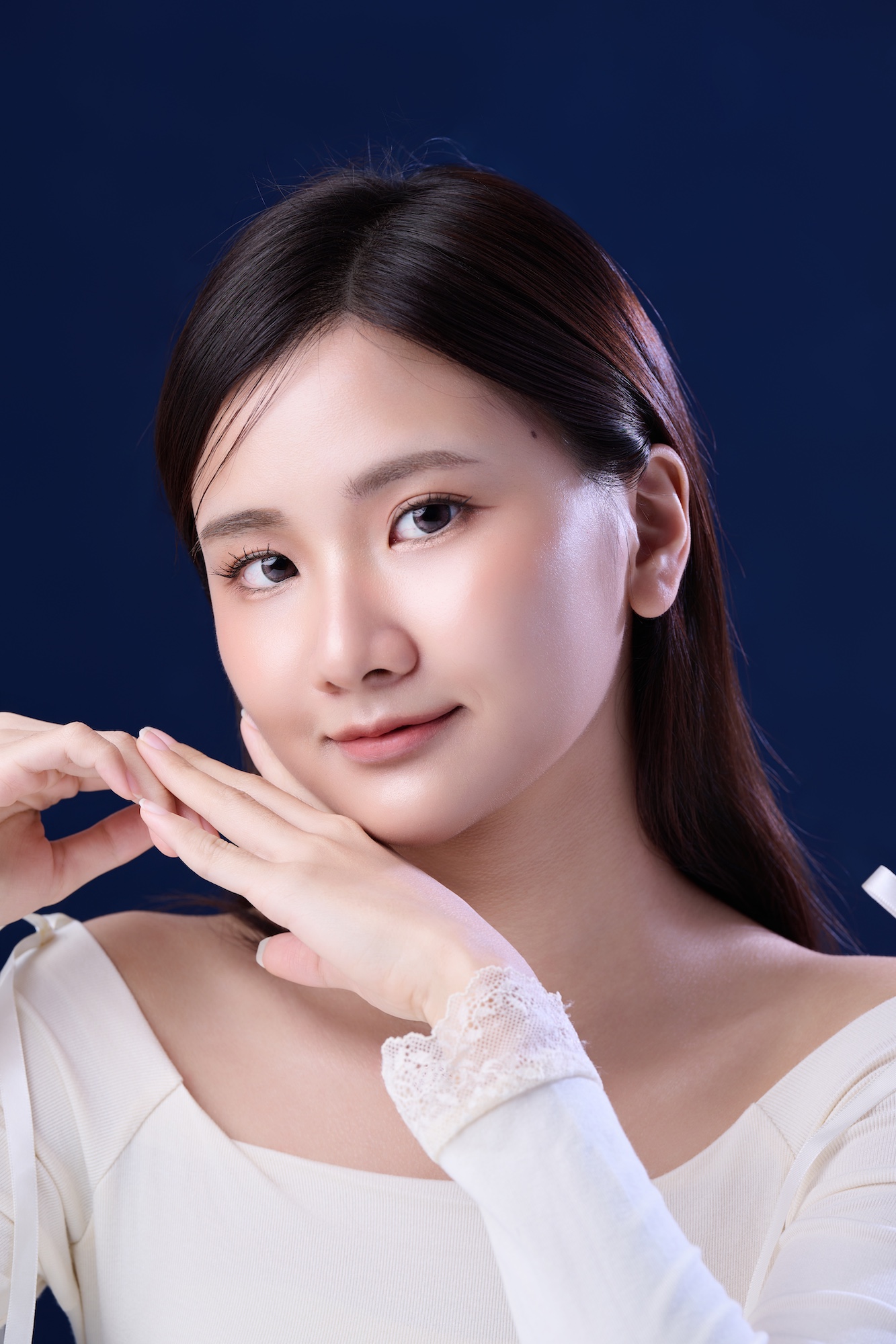 台南形象照推薦：韓系優雅風格女性個人寫真。雙手輕撫臉頰展現溫柔神韻，搭配細膩光影與深藍色背景，呈現高質感通透膚質，適合美妝品牌、藝人頭像與社群經營。