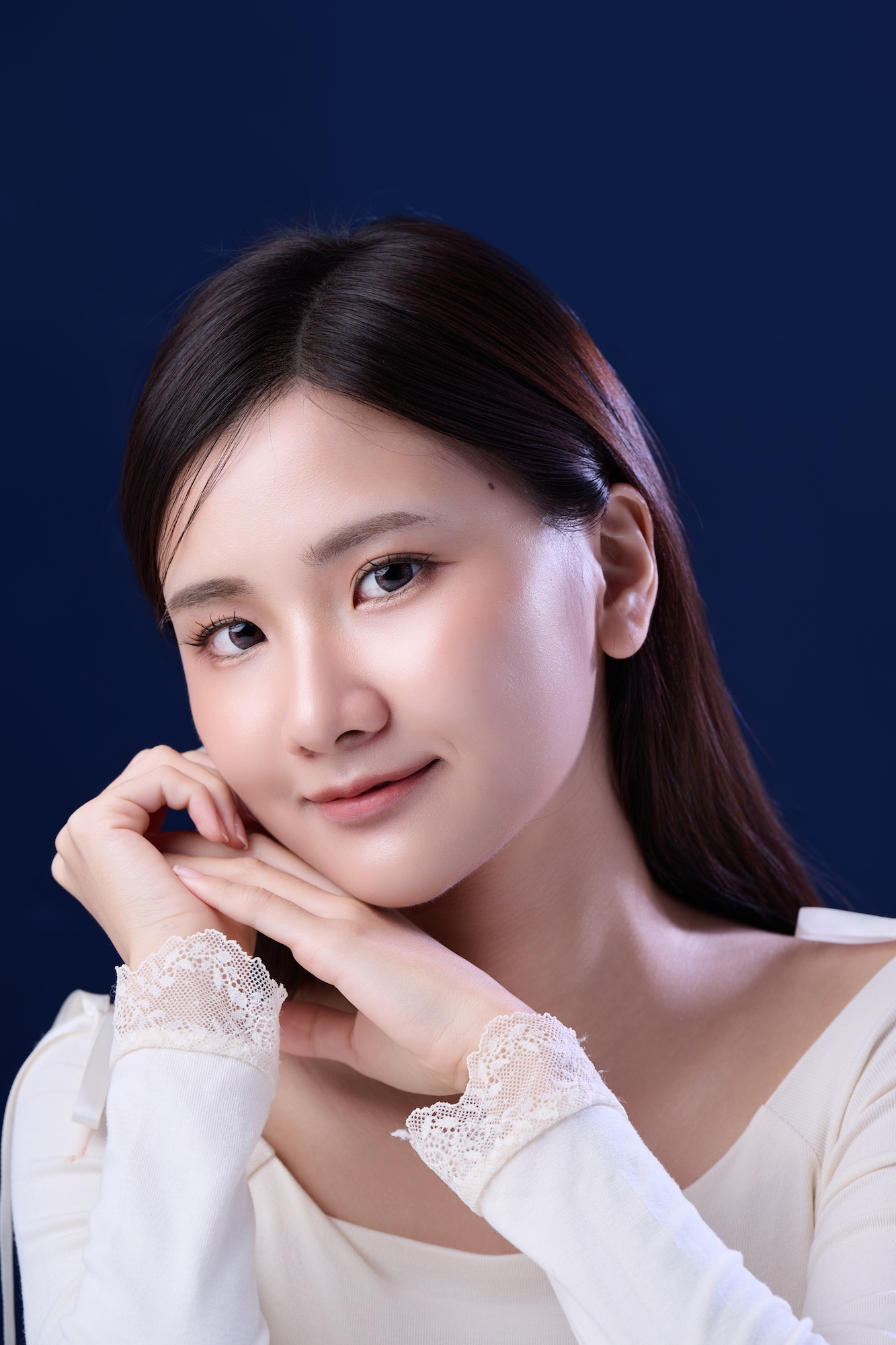 台南形象照推薦：溫柔系韓式肖像攝影。女子雙手輕托臉龐，展現細膩蕾絲袖口細節與清透妝感，深藍色背景突顯個人品牌質感。